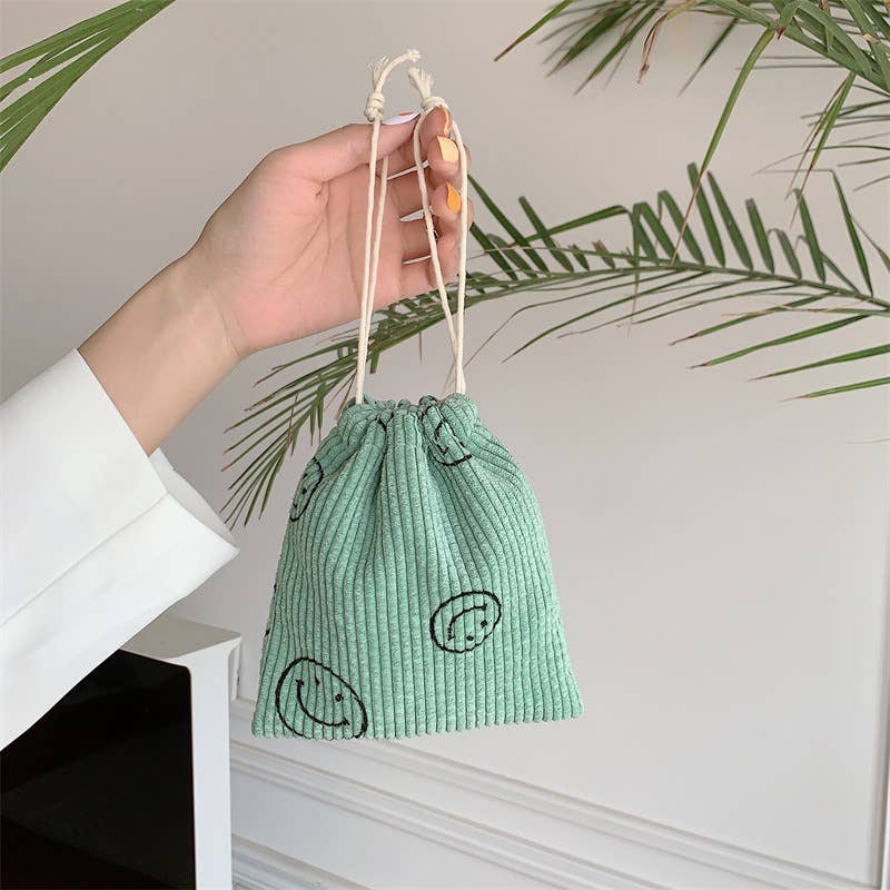 Hand holding a green drawstring bag with black designs against a neutral background