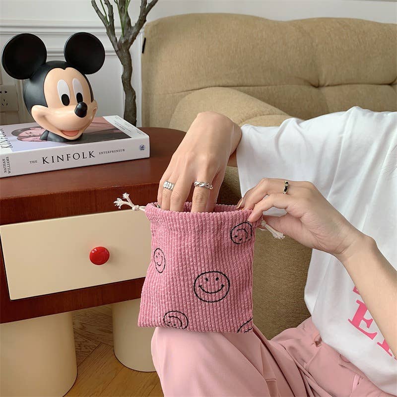 Person holding a pink textured pouch with smiley face patterns, sitting on a beige couch.