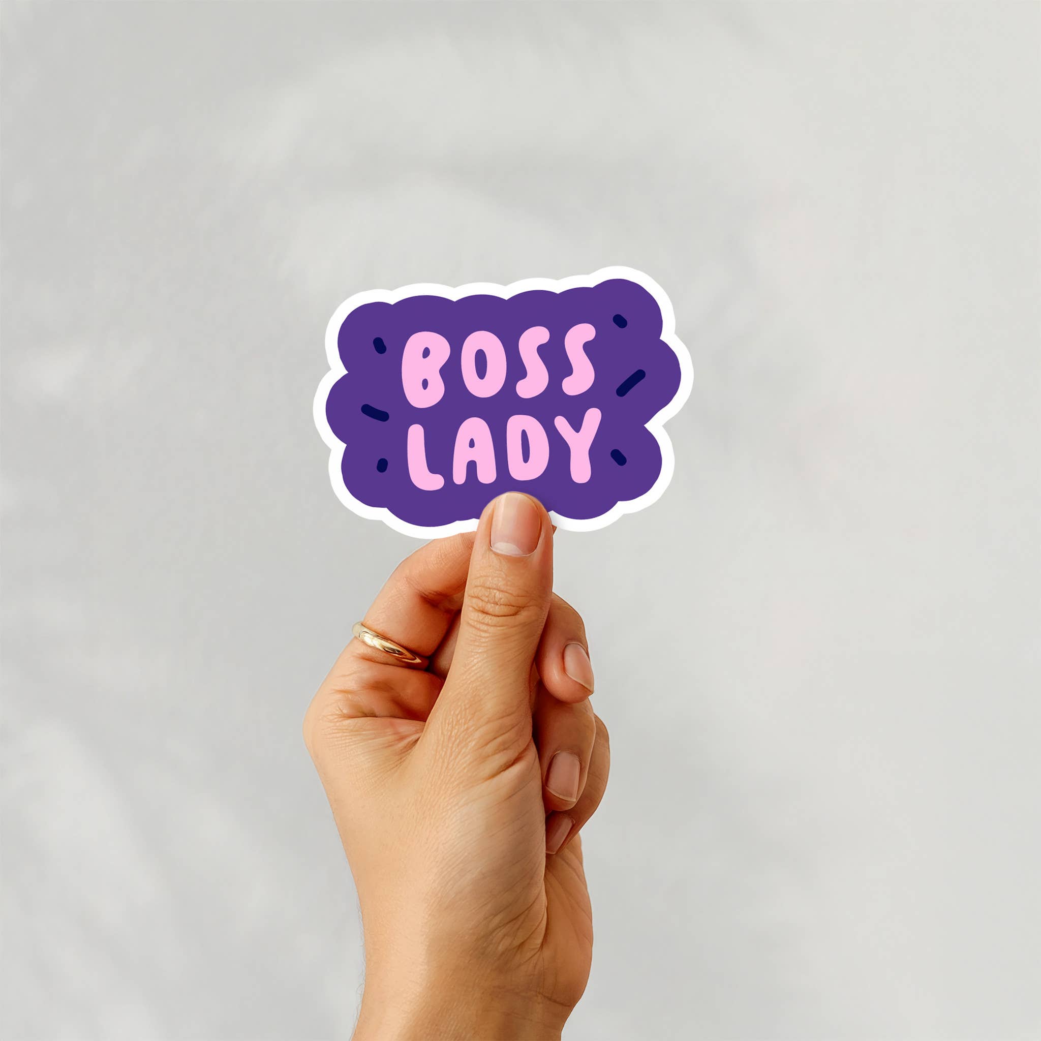 Hand holding a 'BOSS LADY' sticker against a light gray background