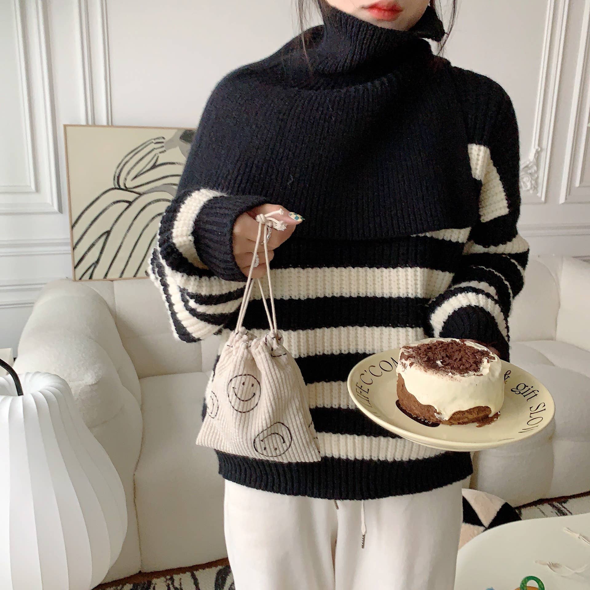 Person wearing a black and white striped sweater holding a plate with a dessert and a small bag.