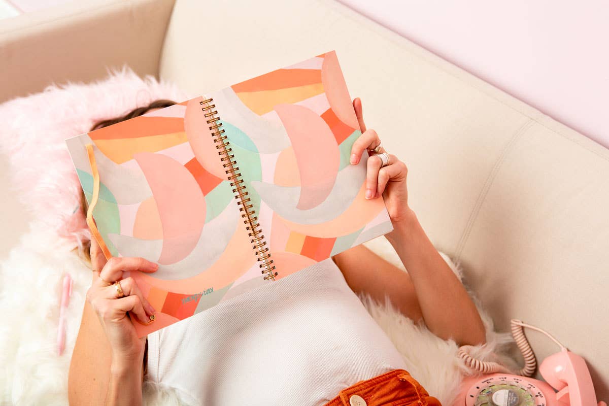 Person holding a colorful spiral-bound notebook on a white couch.