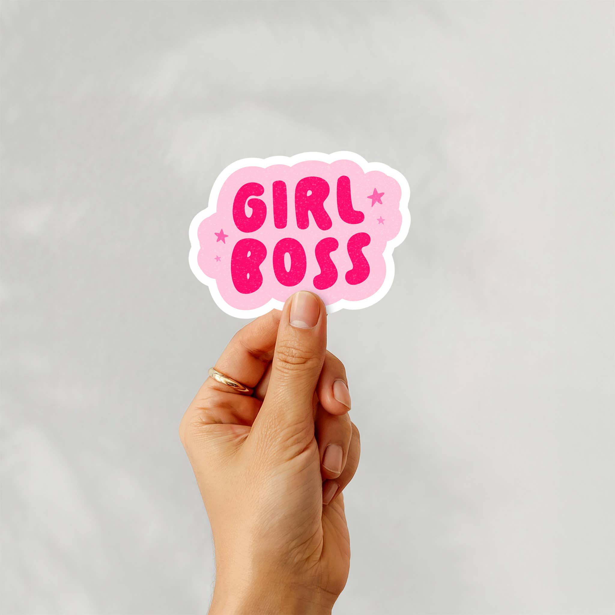 Hand holding a 'Girl Boss' sticker against a light gray background
