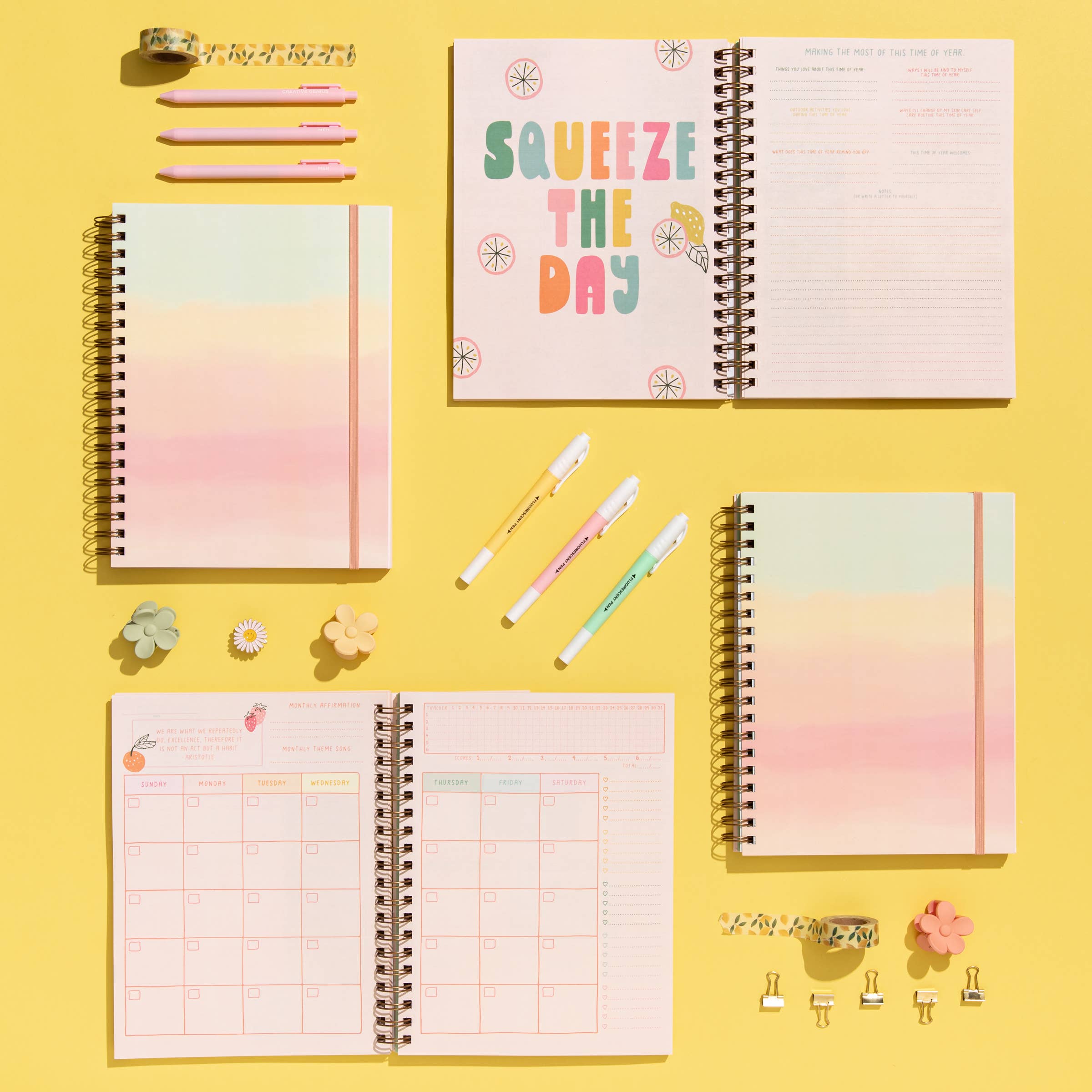 Three spiral-bound planners on a yellow background with colorful pens and decorative items.