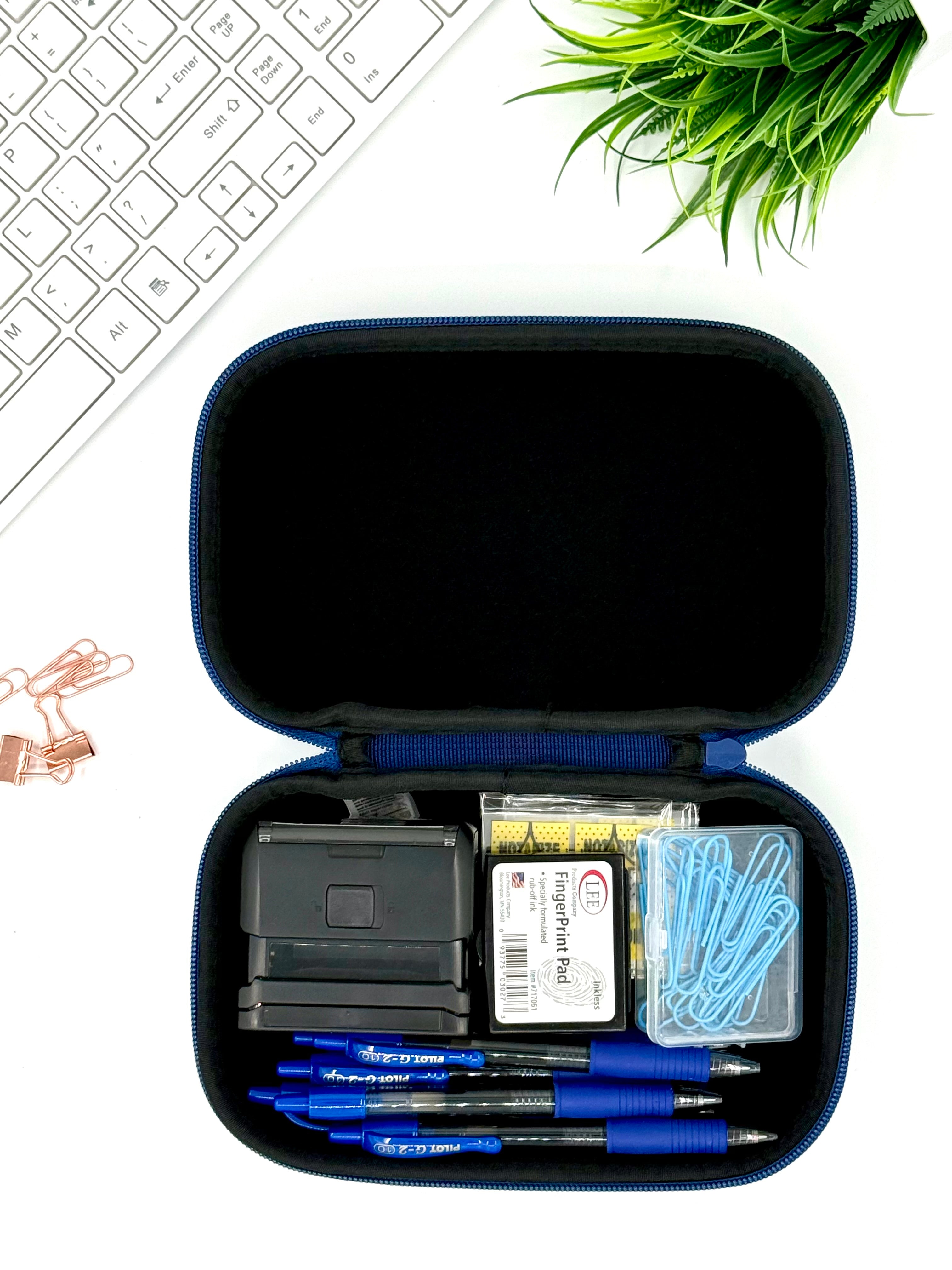 Open blue case with stationery items on a white surface with a keyboard and plant in the background