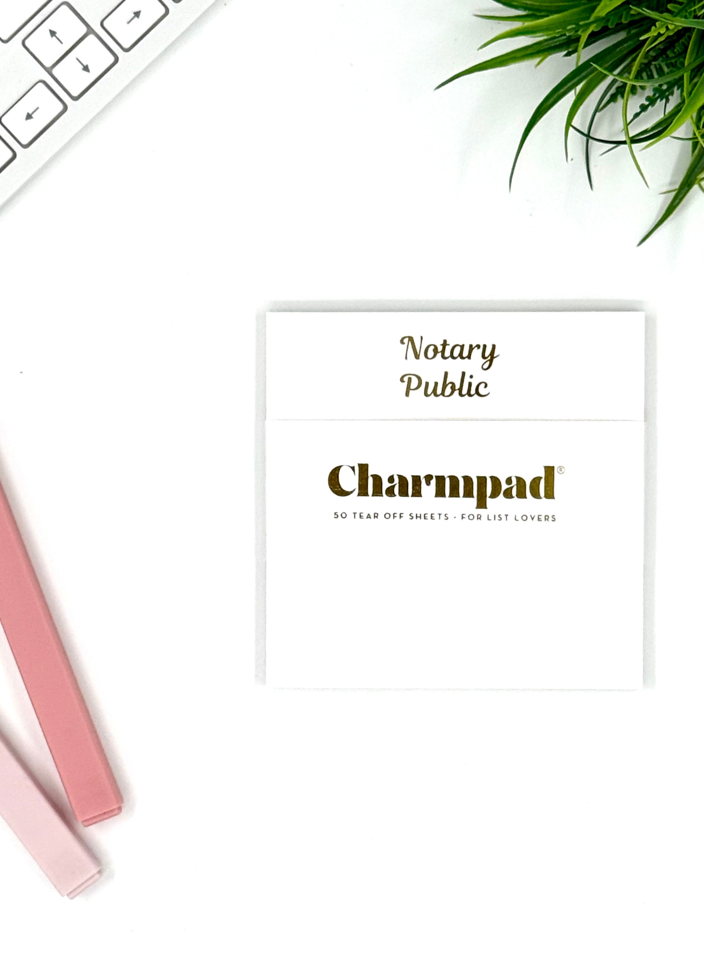 Charmpad notary public desk pad on a white surface with a pen and plant.
