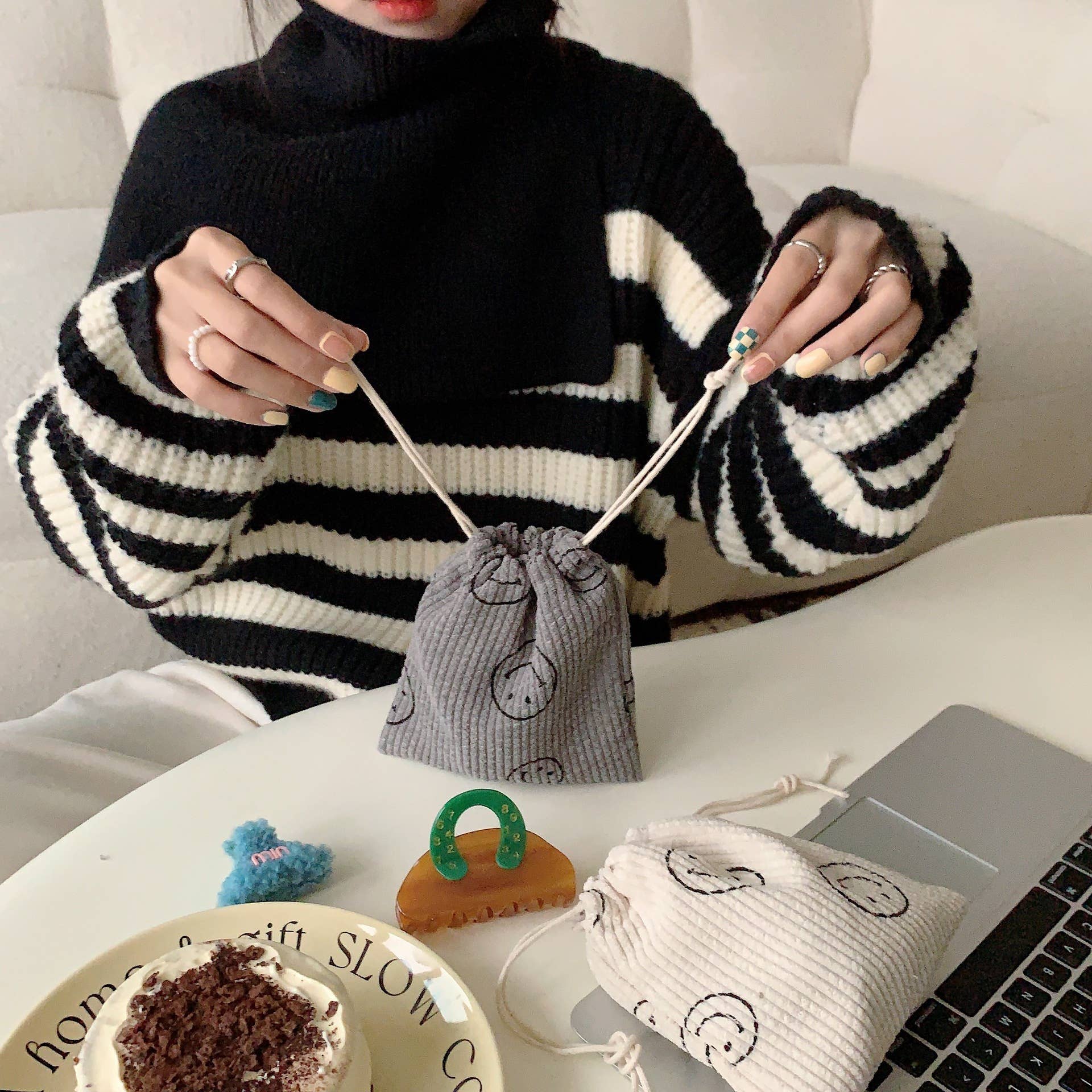 Person wearing a black and white striped sweater with a gray drawstring bag on a table.