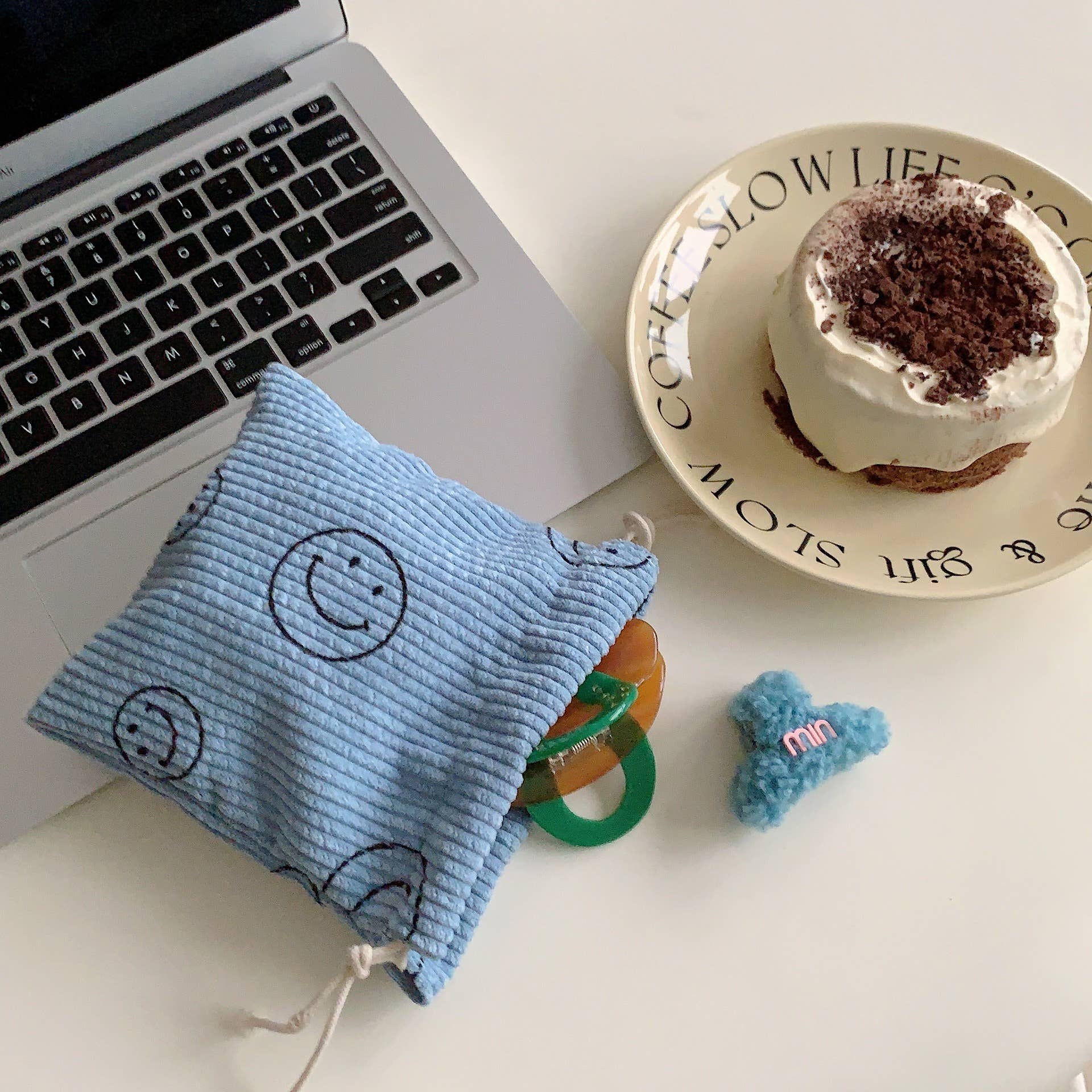 Laptop on a desk with a blue drawstring bag, green pacifier, and small cake.