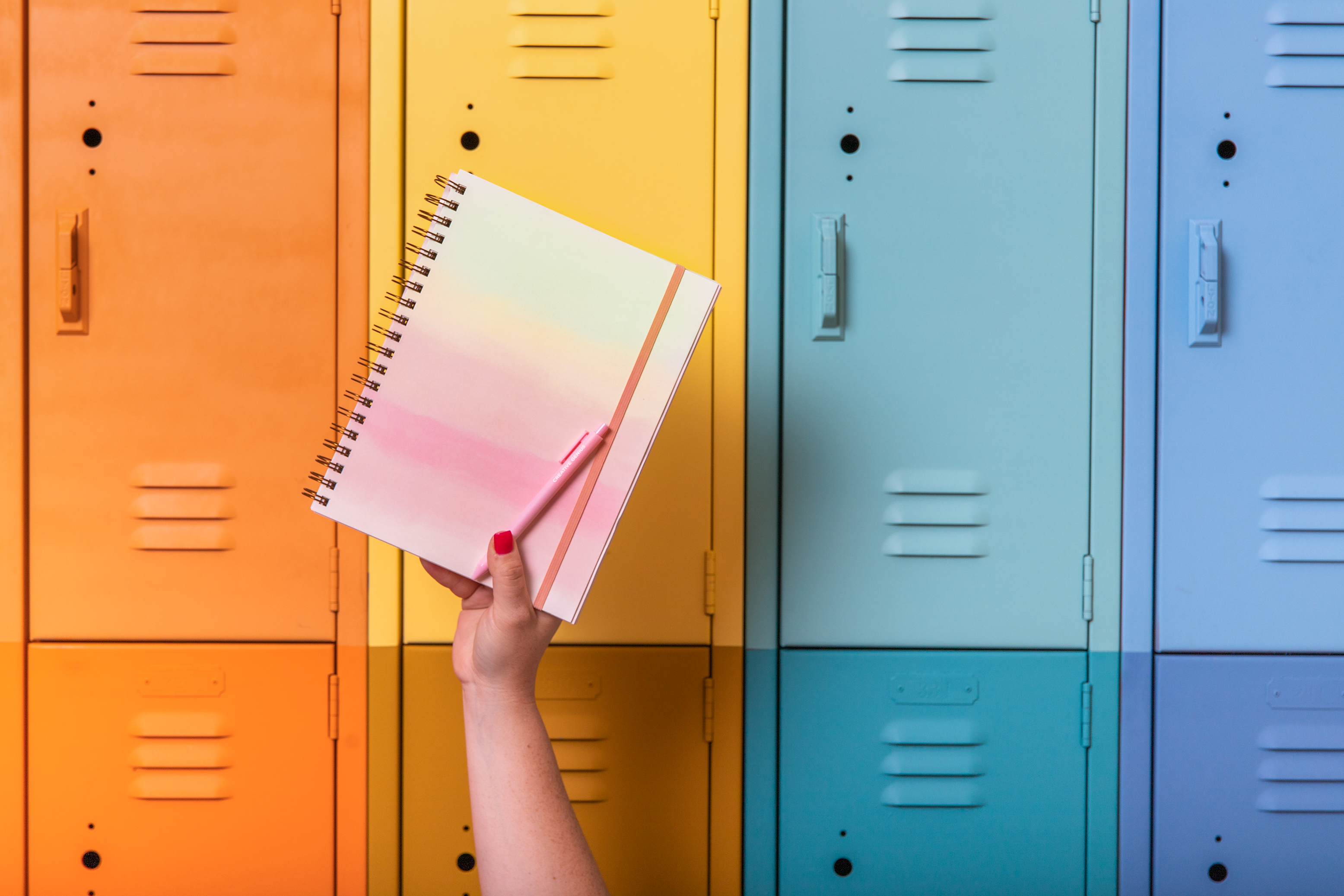 Hand holding a colorful notebook and pen in front of multicolored lockers