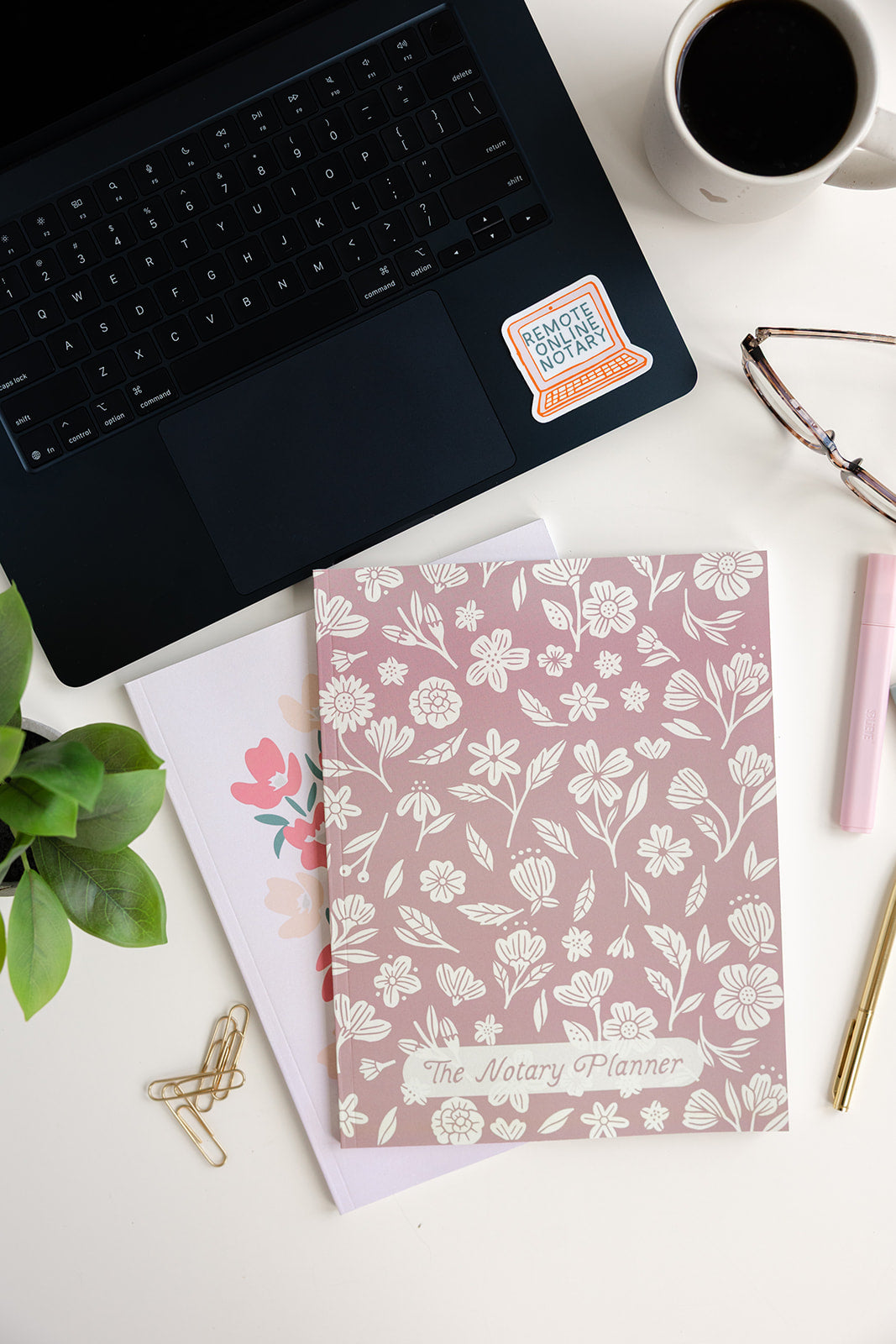 Floral notebook, coffee cup, laptop, and stationery on a white surface
